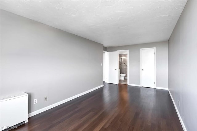 unfurnished bedroom featuring ensuite bathroom, dark hardwood / wood-style flooring, radiator heating unit, and a textured ceiling