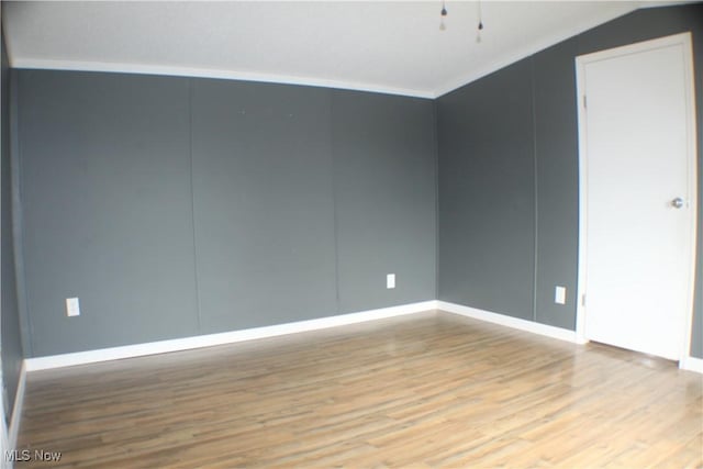 empty room featuring vaulted ceiling, ornamental molding, and light hardwood / wood-style flooring