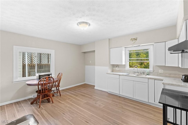 kitchen with white cabinets, a textured ceiling, light hardwood / wood-style flooring, and sink