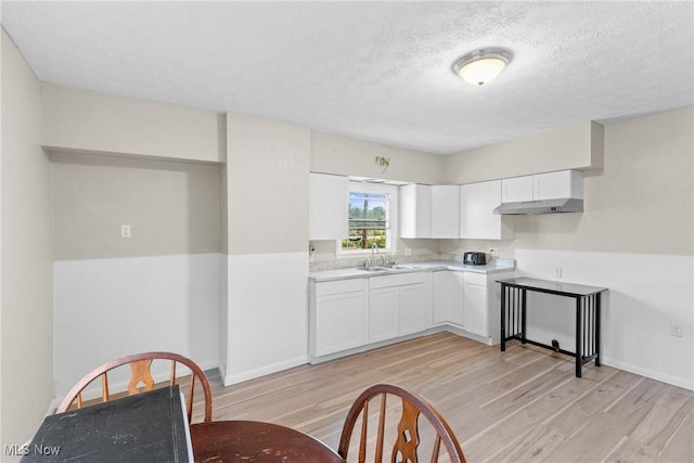 kitchen featuring white cabinetry, sink, a textured ceiling, and light hardwood / wood-style flooring