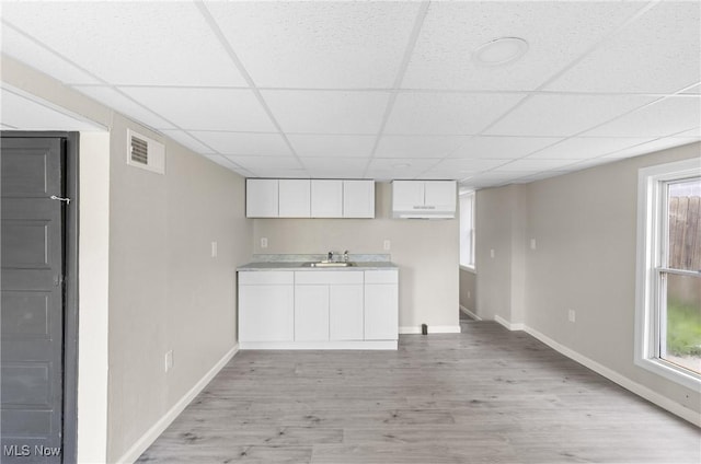 kitchen featuring a paneled ceiling, sink, white cabinets, and light wood-type flooring