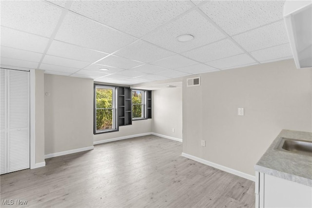 unfurnished living room featuring sink, a drop ceiling, and light wood-type flooring