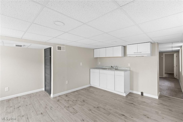 kitchen with white cabinets, light hardwood / wood-style flooring, and a drop ceiling