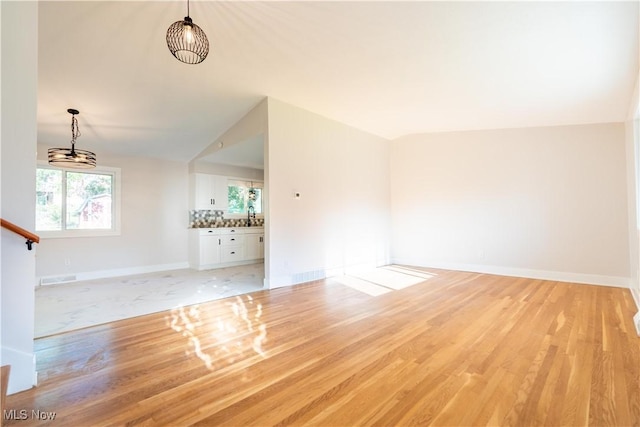 unfurnished living room featuring light wood-type flooring, sink, and vaulted ceiling