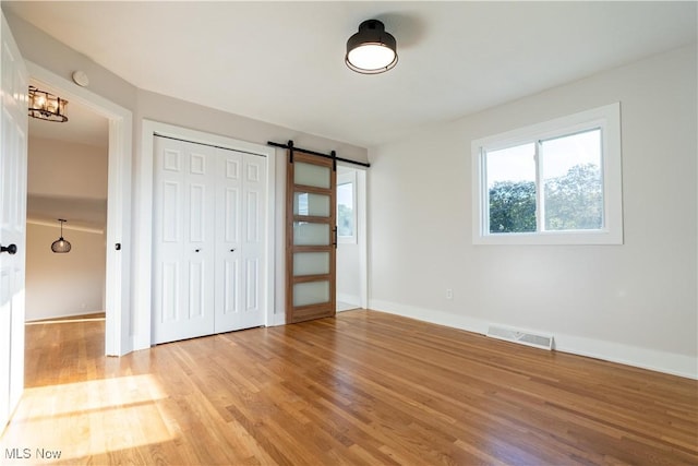 unfurnished bedroom featuring a barn door, light hardwood / wood-style flooring, and a closet