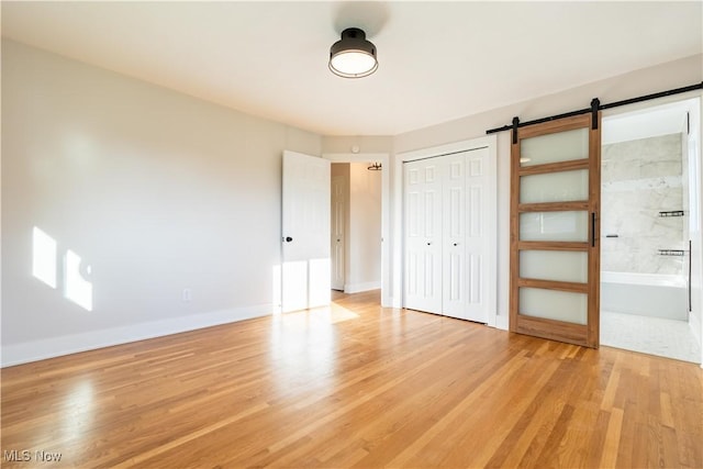 unfurnished bedroom featuring a barn door, ensuite bathroom, light hardwood / wood-style flooring, and a closet