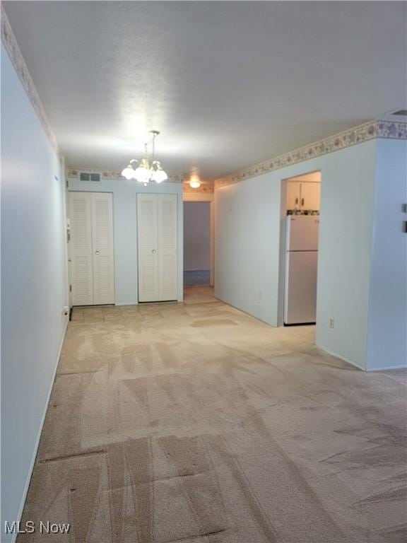 spare room featuring a notable chandelier and light colored carpet