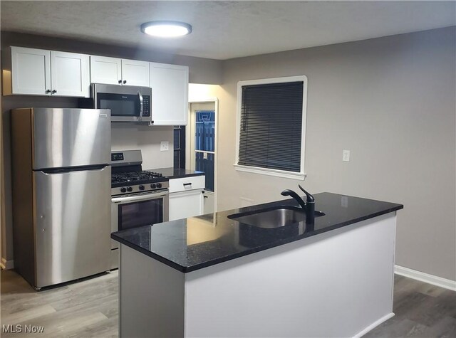 kitchen with stainless steel appliances, sink, hardwood / wood-style flooring, a center island with sink, and white cabinetry