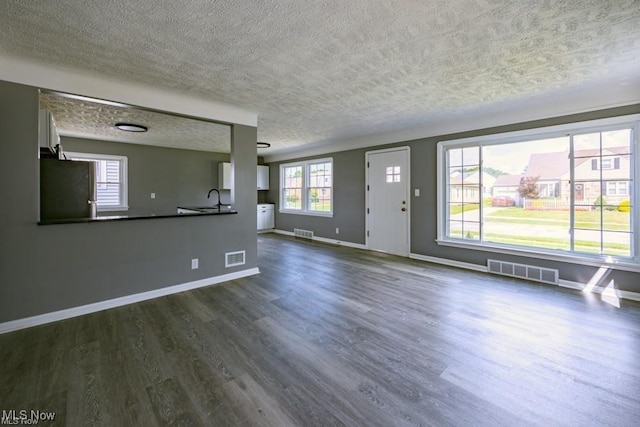 unfurnished living room featuring dark wood-type flooring, sink, and a textured ceiling