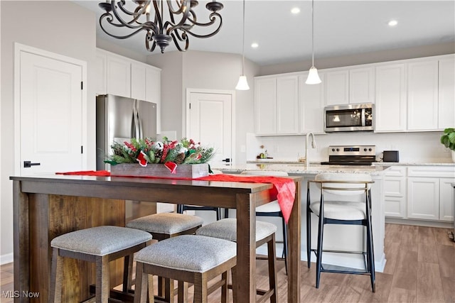 kitchen with white cabinetry, stainless steel appliances, an island with sink, decorative light fixtures, and light wood-type flooring