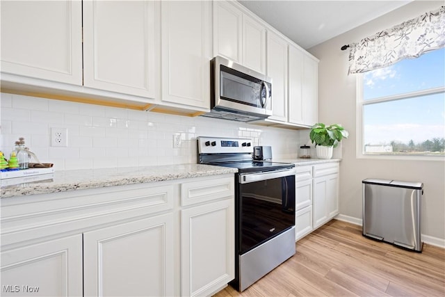 kitchen with decorative backsplash, light hardwood / wood-style floors, light stone counters, white cabinetry, and stainless steel appliances