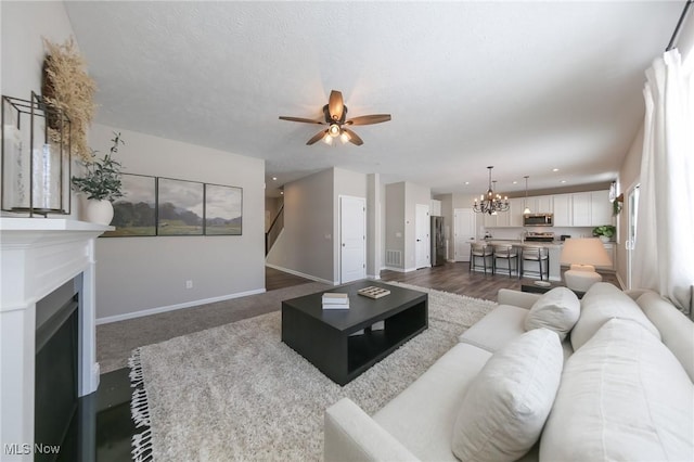 living area with stairway, baseboards, ceiling fan with notable chandelier, a fireplace with flush hearth, and a textured ceiling