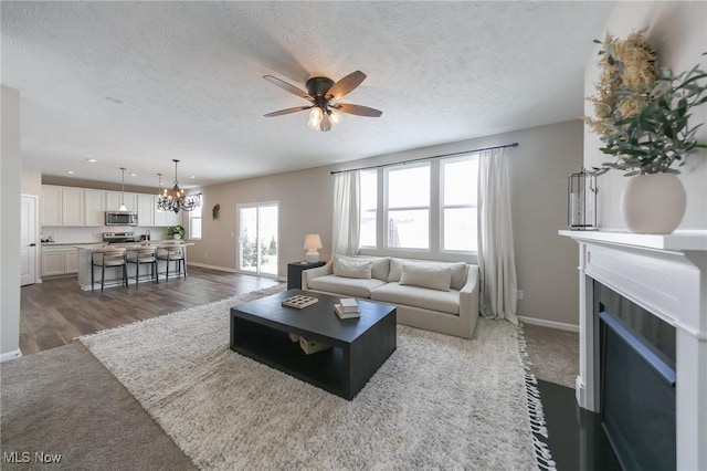 living area with baseboards, ceiling fan with notable chandelier, a fireplace with flush hearth, and a textured ceiling