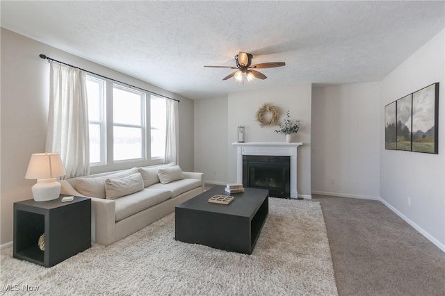 living area featuring a ceiling fan, baseboards, a textured ceiling, a fireplace, and carpet floors