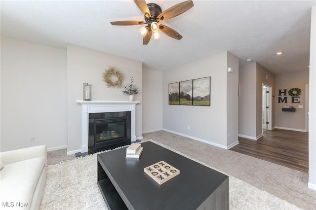 carpeted living area featuring baseboards, a ceiling fan, and a fireplace with flush hearth