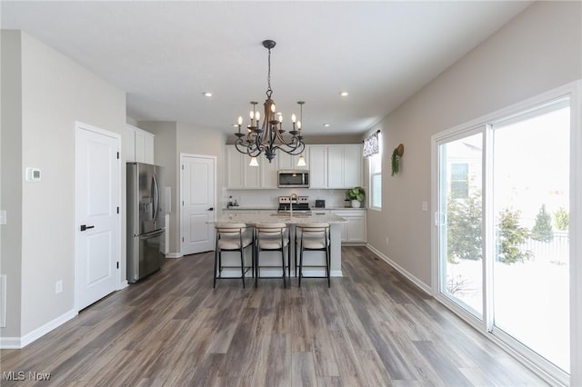 kitchen featuring a breakfast bar area, a center island with sink, appliances with stainless steel finishes, decorative light fixtures, and white cabinetry