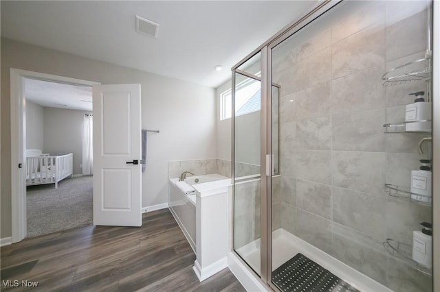 full bathroom featuring wood finished floors, visible vents, a garden tub, a shower stall, and baseboards