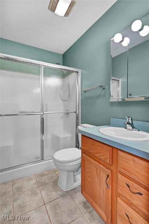 bathroom featuring vanity, tile patterned flooring, toilet, a textured ceiling, and walk in shower