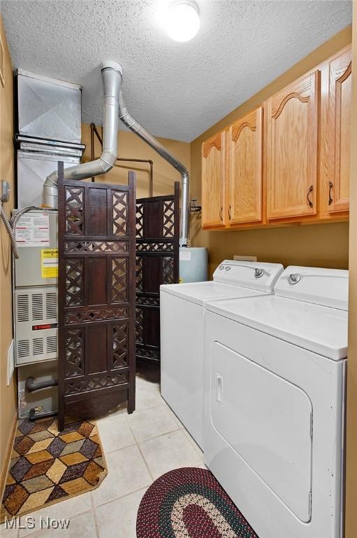 clothes washing area featuring cabinets, independent washer and dryer, a textured ceiling, and light tile patterned floors