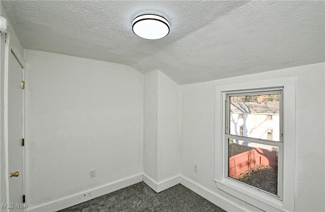 bonus room featuring dark colored carpet, a textured ceiling, and lofted ceiling