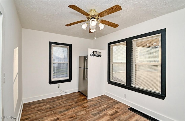 empty room featuring a wealth of natural light, a textured ceiling, ceiling fan, and dark wood-type flooring