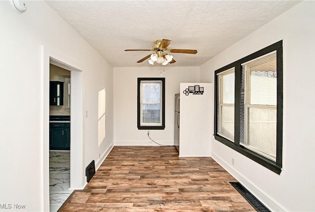 unfurnished dining area with ceiling fan, a textured ceiling, and hardwood / wood-style flooring