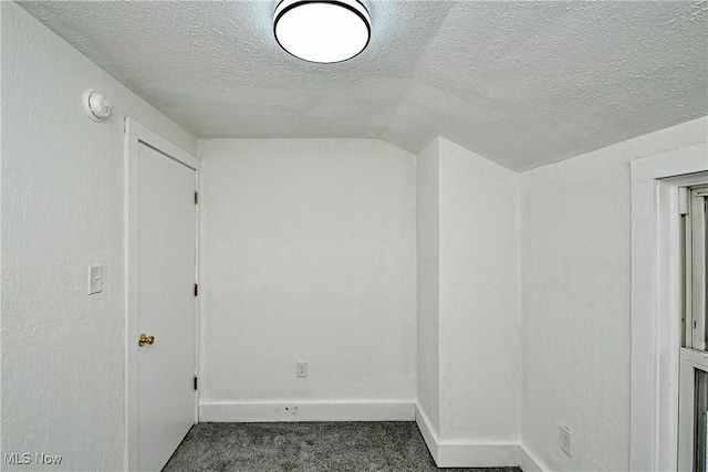 empty room featuring a textured ceiling, vaulted ceiling, and dark colored carpet