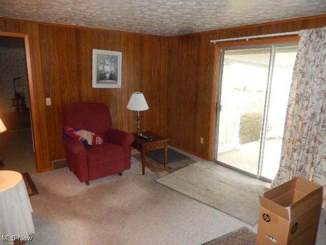 sitting room with carpet, a textured ceiling, and wooden walls