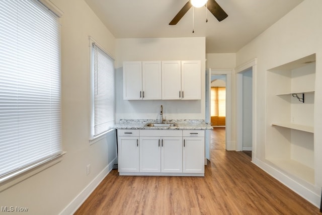 kitchen with light stone countertops, light wood-type flooring, ceiling fan, sink, and white cabinetry