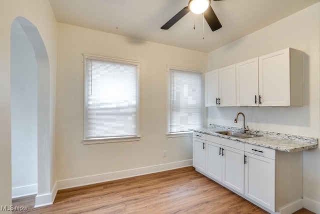 kitchen with ceiling fan, sink, light stone countertops, white cabinets, and light wood-type flooring