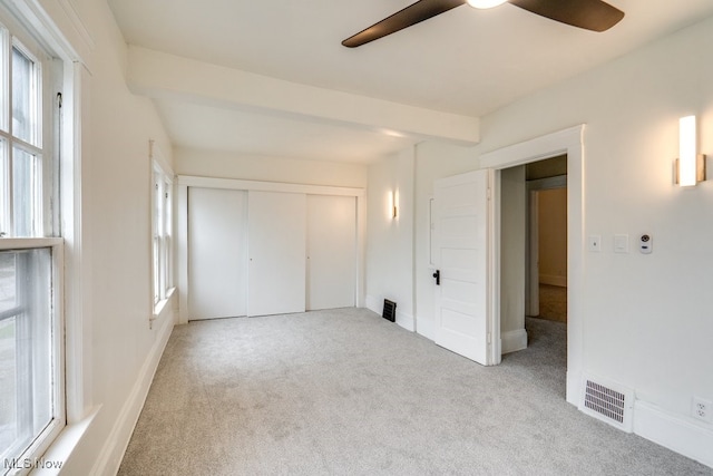 unfurnished bedroom featuring multiple windows, a closet, ceiling fan, and light colored carpet