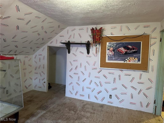 unfurnished bedroom with wood-type flooring, lofted ceiling, and a textured ceiling