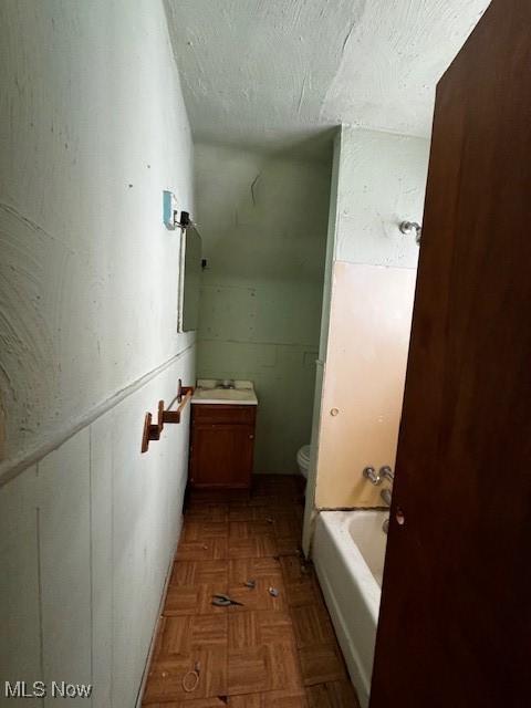 bathroom featuring a washtub, toilet, parquet flooring, and a textured ceiling