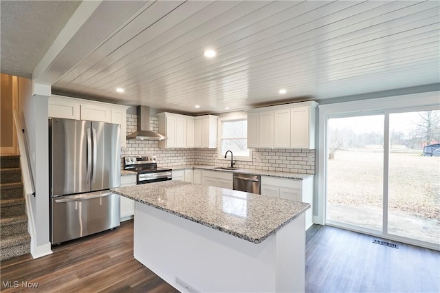 kitchen with white cabinetry, sink, stainless steel appliances, wall chimney range hood, and a kitchen island