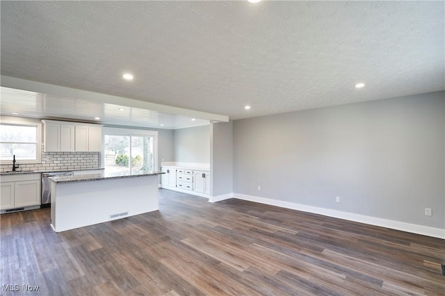 kitchen with light stone countertops, a center island, dark hardwood / wood-style floors, backsplash, and white cabinets