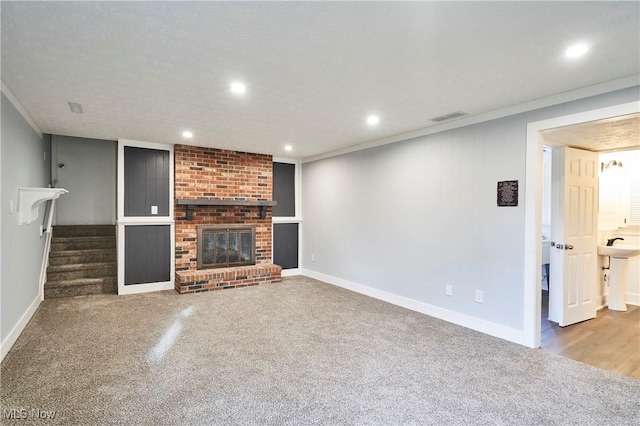 unfurnished living room featuring carpet floors, ornamental molding, a textured ceiling, and a brick fireplace