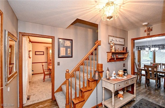 stairway with wood-type flooring, a textured ceiling, and a notable chandelier