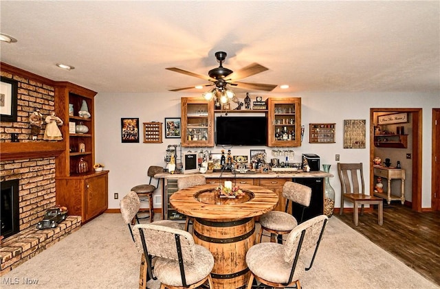 carpeted dining area with a textured ceiling, ceiling fan, a fireplace, and indoor bar