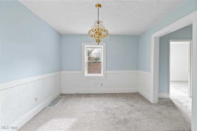 spare room featuring carpet, a chandelier, and a textured ceiling