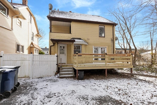 snow covered back of property with a wooden deck