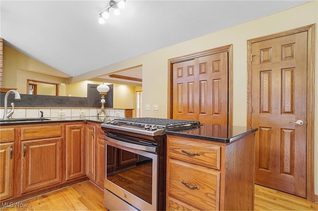 kitchen featuring tasteful backsplash, stainless steel range with gas cooktop, sink, and light hardwood / wood-style flooring