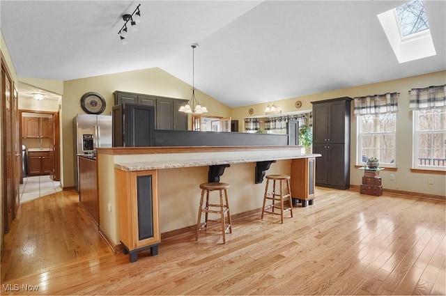 kitchen featuring stainless steel fridge, a breakfast bar, lofted ceiling with skylight, an inviting chandelier, and light hardwood / wood-style flooring