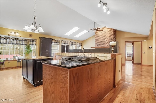 kitchen featuring pendant lighting, a center island, ceiling fan with notable chandelier, light hardwood / wood-style flooring, and vaulted ceiling with skylight