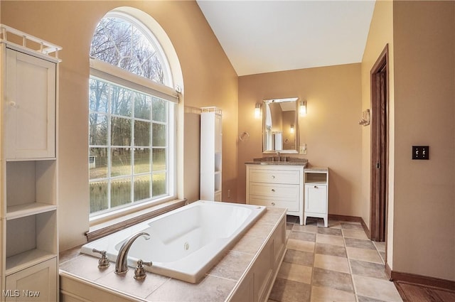 bathroom featuring vanity, tiled tub, and vaulted ceiling