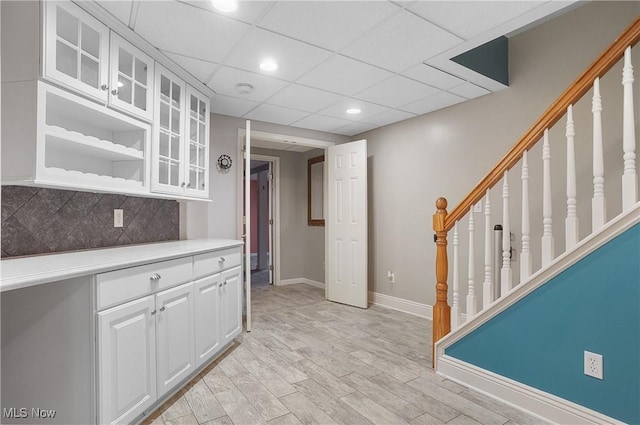 interior space with tasteful backsplash, white cabinetry, a drop ceiling, and light hardwood / wood-style flooring