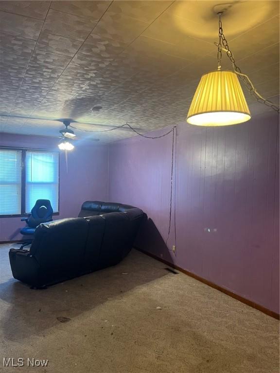 carpeted living room featuring ceiling fan and wood walls