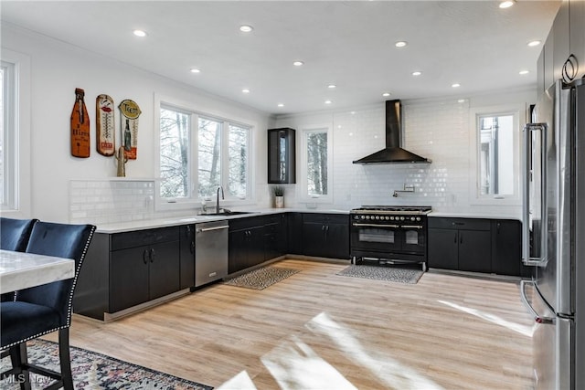 kitchen with sink, wall chimney range hood, tasteful backsplash, high quality appliances, and light wood-type flooring