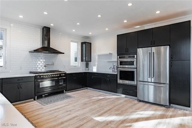 kitchen with wall chimney exhaust hood, premium appliances, light hardwood / wood-style floors, and decorative backsplash