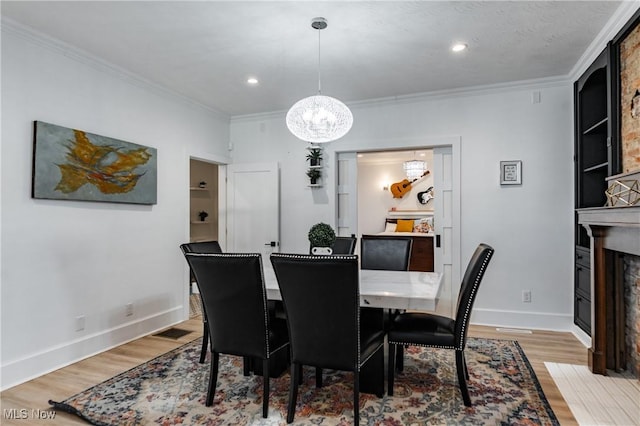 dining area with a fireplace, light wood-type flooring, crown molding, and a chandelier