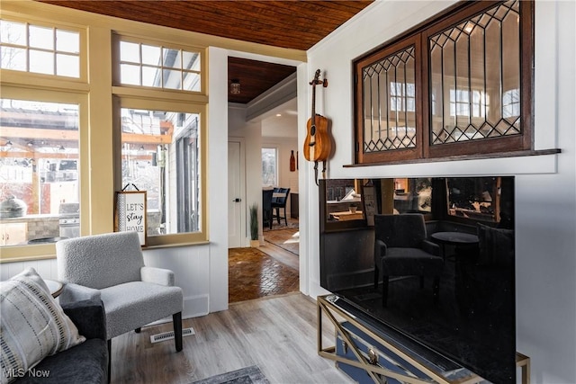 living room with ornamental molding, wooden ceiling, and light wood-type flooring